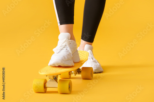 Sporty young woman with skateboard on color background, closeup