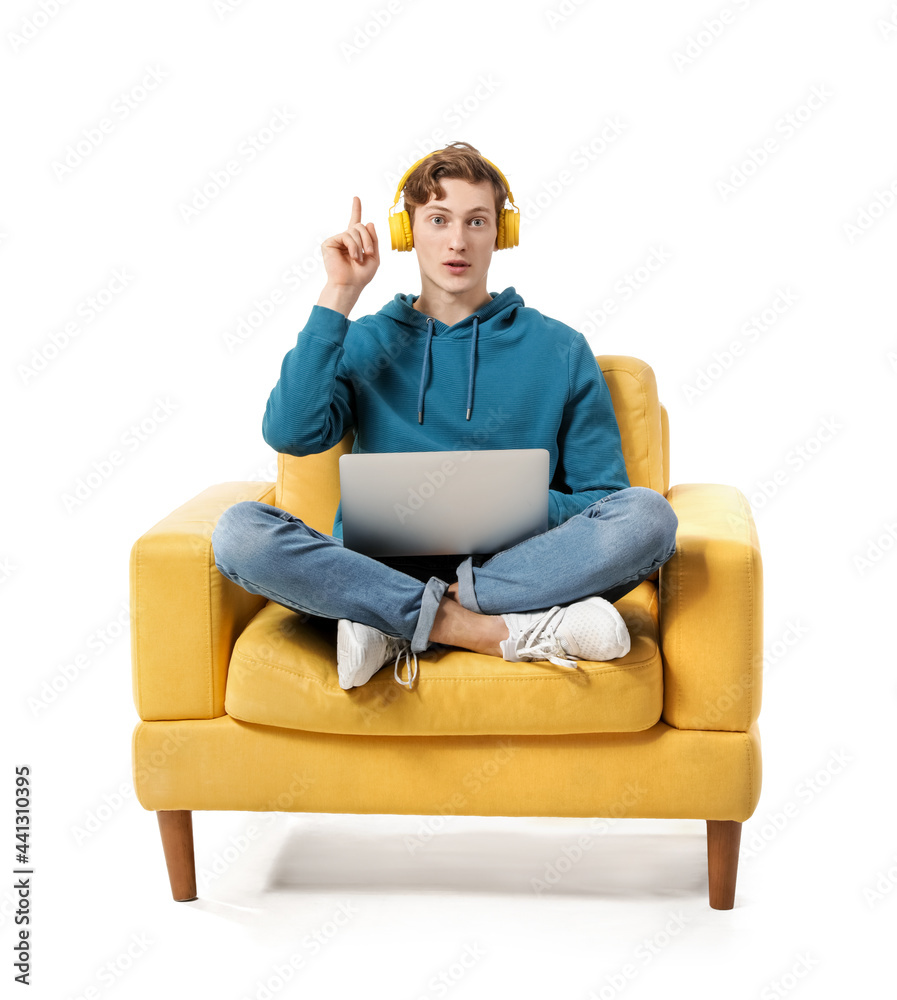 Young man with laptop and raised index finger listening to music while sitting in armchair on white background Young man with laptop and raised index finger listening to music while sitting in armchair on white background