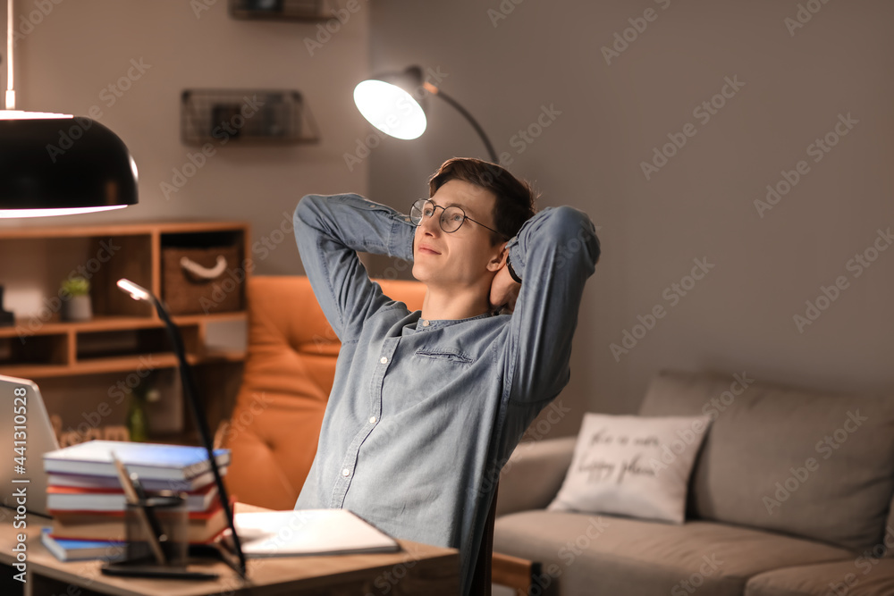Fototapeta premium Young man resting after studying at home in evening