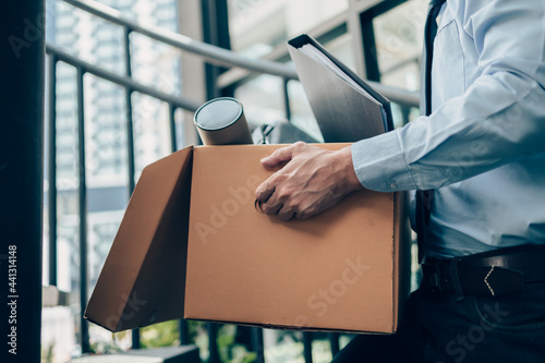 Unemployed hold cardboard box and laptop bag, dossier and drawing tube in box. Quiting a job, businessman fired or leave a job concpet. photo