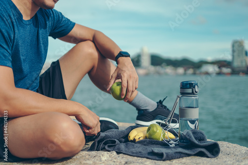 Healthy man hold apple fruit and sitting on the stone near the beach.