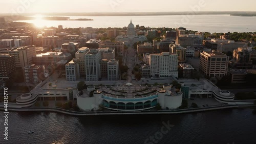 Aerial above the lake towards city street leading to domed Wisconsin State Capitol building in Madison with sun reflect off water of Lake Mendota, Wisconsin. Warm sunset light	 photo