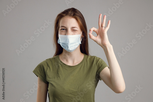 Studio profile portrait of a young blonde in a medical flu mask on a grey background with a copy space. A medical theme with an empty background.