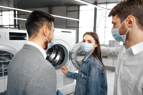 Salesman in hypermarket wearing medical mask demonstrates his clients a new washing machine