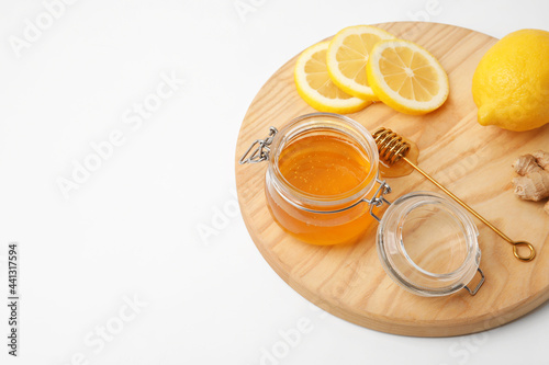 Glass jar with sweet honey  lemon slices and ginger on wooden board against white background