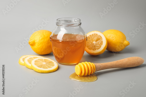 Glass jar with sweet honey, dipper and lemons on grey background