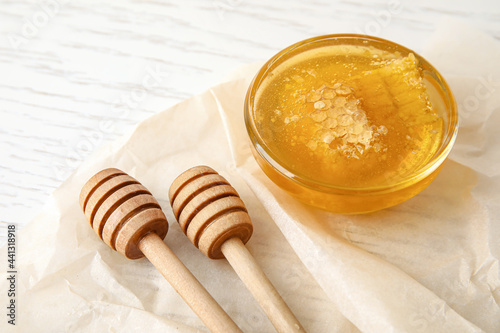 Glass bowl with sweet honey and dippers on light wooden background, closeup