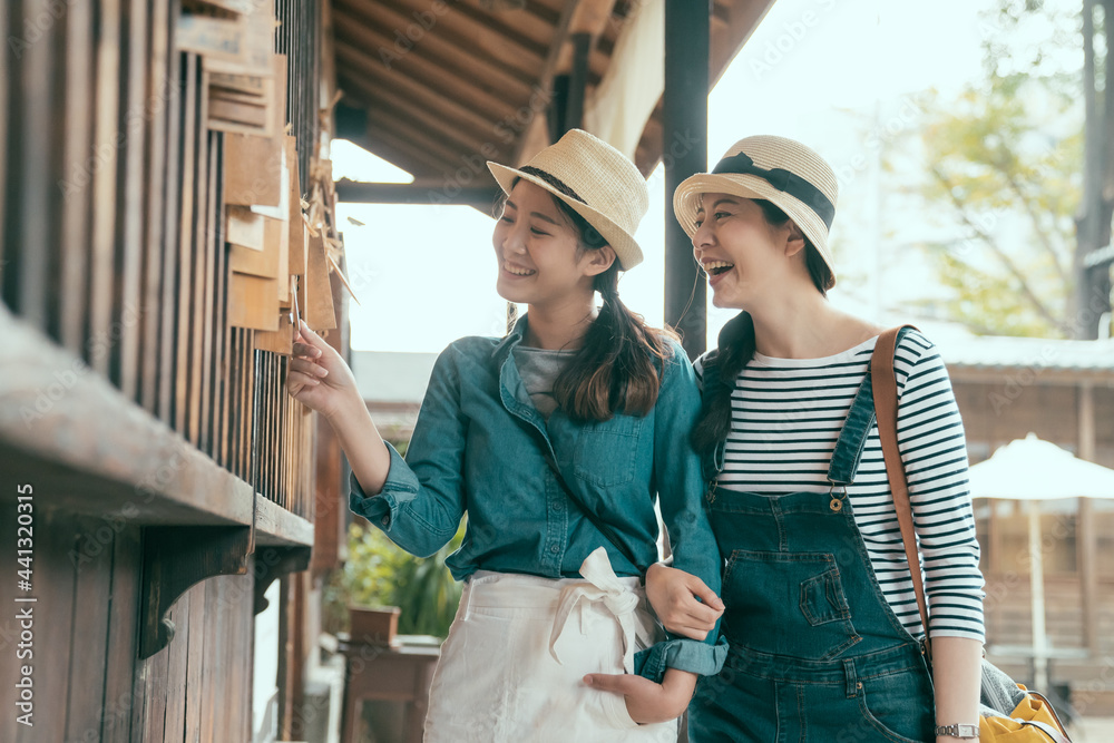 best friends enjoying time together visiting old city in kyoto japan. happy two girl sisters walking in walkway outdoors looking and touching wooden board hanging on window. women reading wishes.