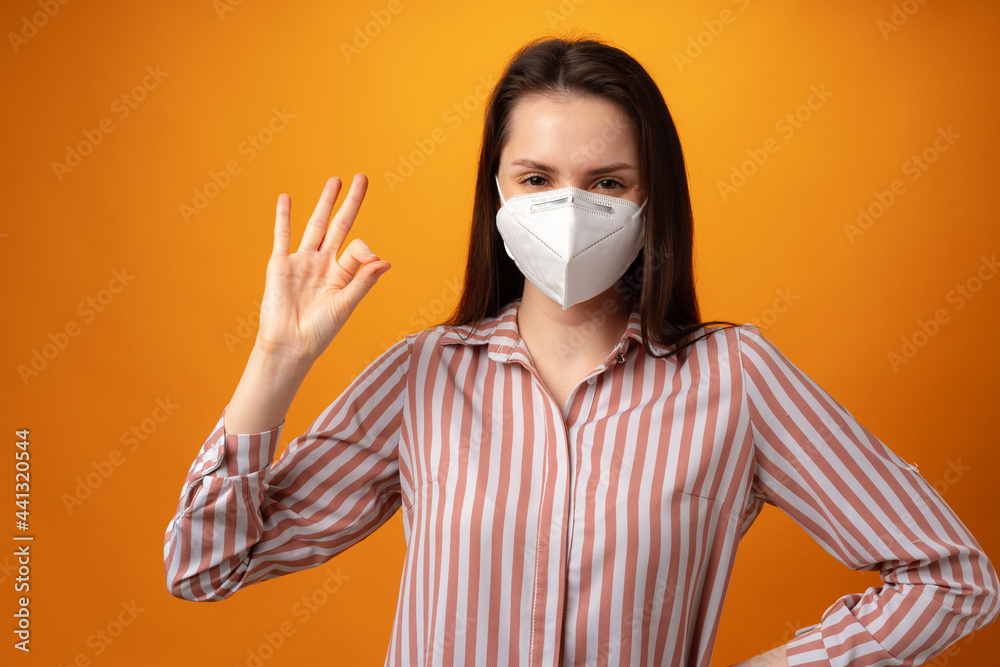 Studio portrait of a young beautiful woman wearing medical face mask against yellow background Studio portrait of a young beautiful woman wearing medical face mask against yellow background
