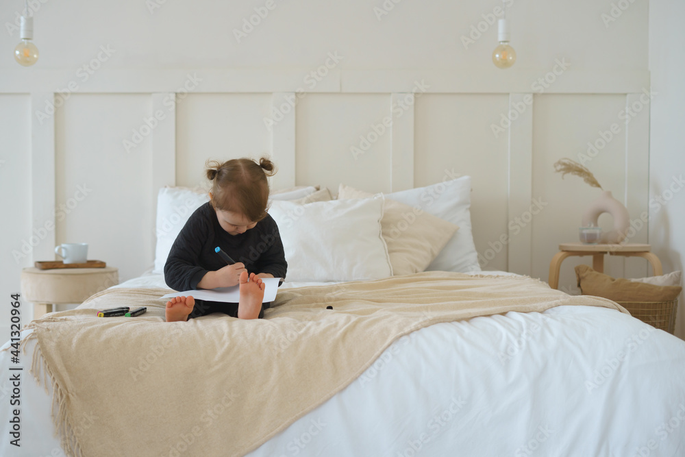 a little girl in black home clothes is sitting on the bed and drawing with felt-tip pens a little girl in black home clothes is sitting on the bed and drawing with felt-tip pens
