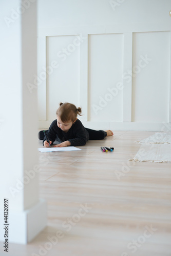 a little girl in black home clothes and barefoot lies on the floor and draws with felt-tip pens on a piece of paper