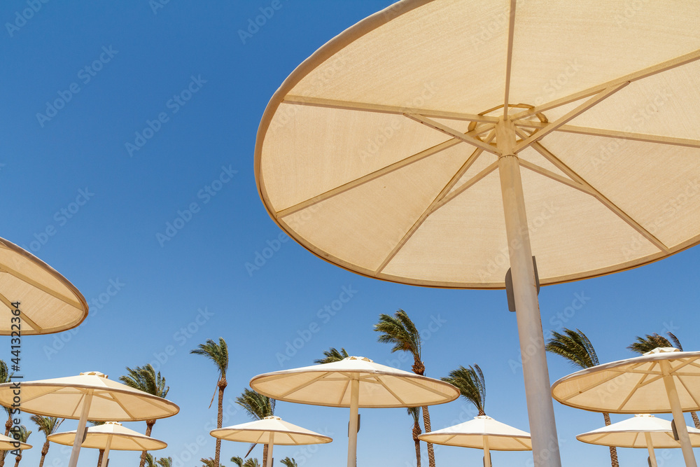 Beach with beige umbrellas against the blue sky.