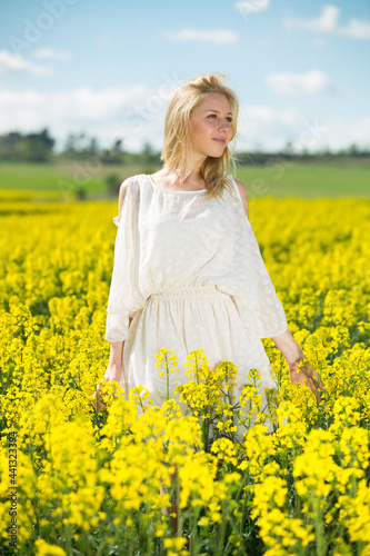 Young woman in yellow oilseed rape field posing in white dress outdoor © JackF