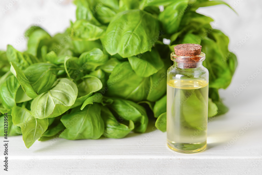 Fresh basil leaves and bottle of essential oil on light wooden background Fresh basil leaves and bottle of essential oil on light wooden background