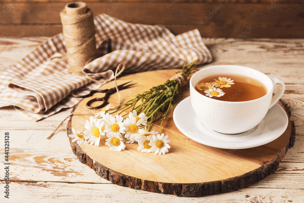Composition with cup of chamomile tea and flowers on light wooden background Composition with cup of chamomile tea and flowers on light wooden background
