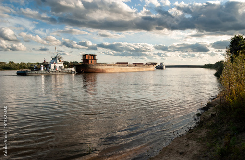 Tugboats are hauling an old barge for scrap. A large river, blue sky and clouds. Oka River, Ryazan region, Russia.