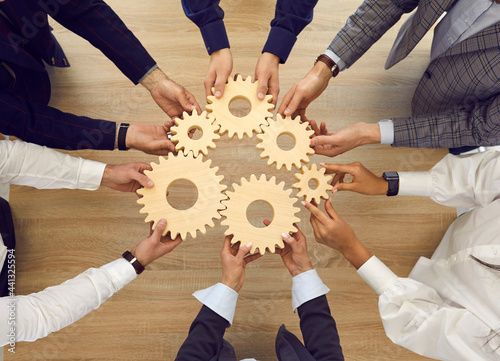 Professional business team connecting cogwheels as metaphor for good teamwork, synergy, effective cooperation and management. High angle, from above, top view closeup shot of human hands holding cogs photo