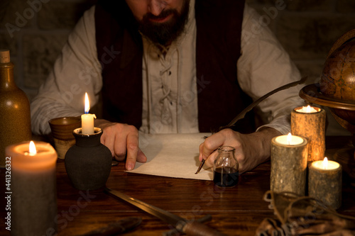 Medieval table with candles and a scroll, man writes with quill and ink