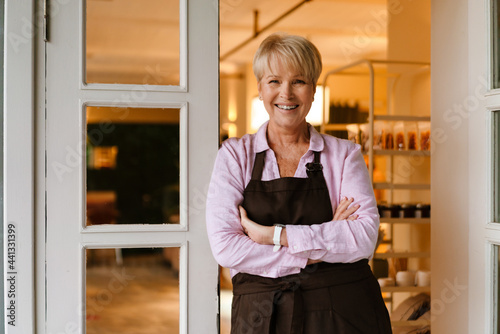 Mature woman smiling at camera while standing in cafe doorway