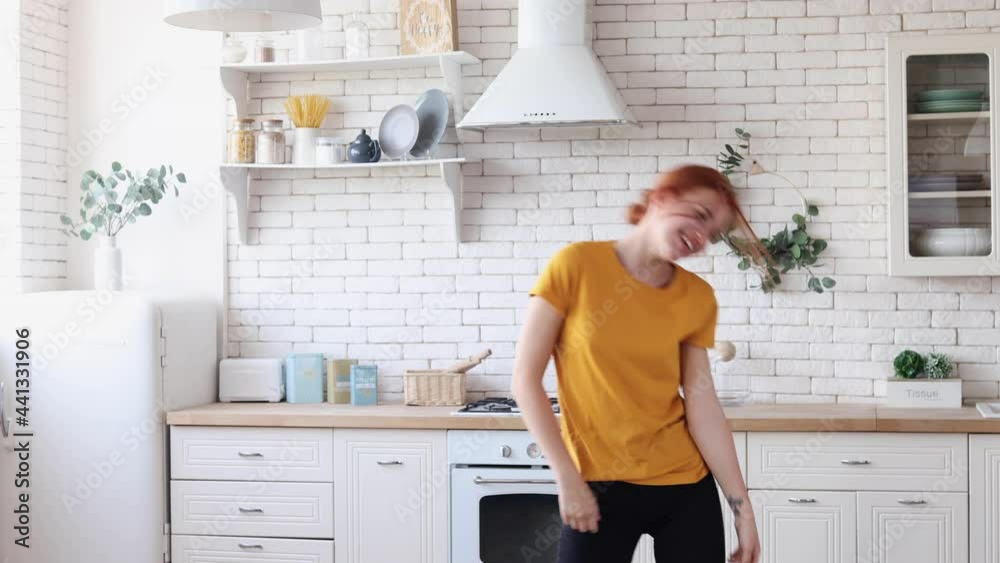 Joyful young red-haired girl dancing in the kitchen in her first house, purchase of first housing concept Joyful young red-haired girl dancing in the kitchen in her first house, purchase of first housing concept