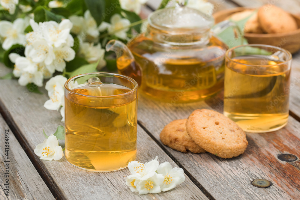 Green Chinese tea with jasmine in mugs and a teapot on a wooden table top with a bouquet of jasmine flowers. Green Chinese tea with jasmine in mugs and a teapot on a wooden table top with a bouquet of jasmine flowers.