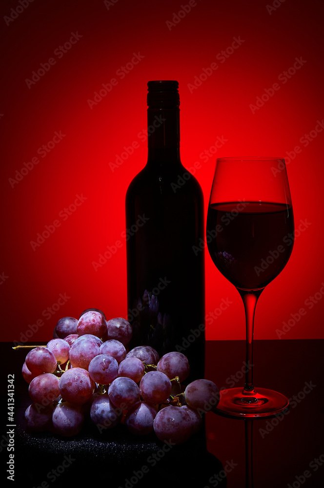 Fototapeta premium Wine bottle glass and bunch of grapes on dark background