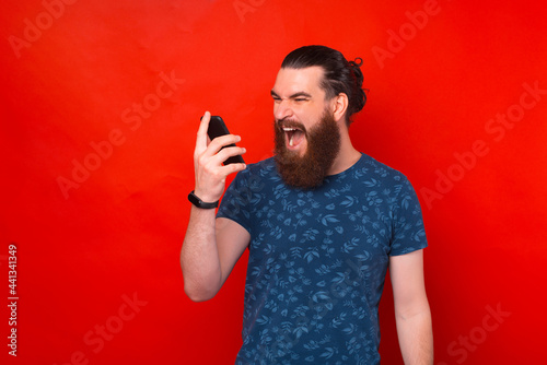 Young bearded hipster man screaming at smartphone over red background © Vulp