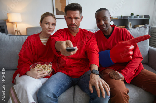 Group of sports fans wearing red while watching game match at home and sitting on sofa