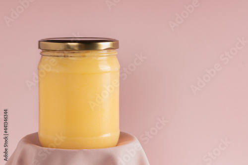 Ghee or clarified butter in jar on pink background. Minimal style. Scene with geometric shapes. Copy space.