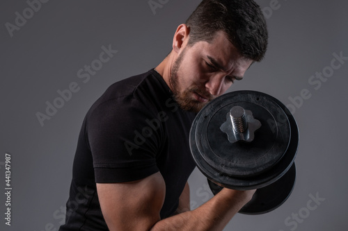 Concentrated young man doing bicep curls with dumbell
