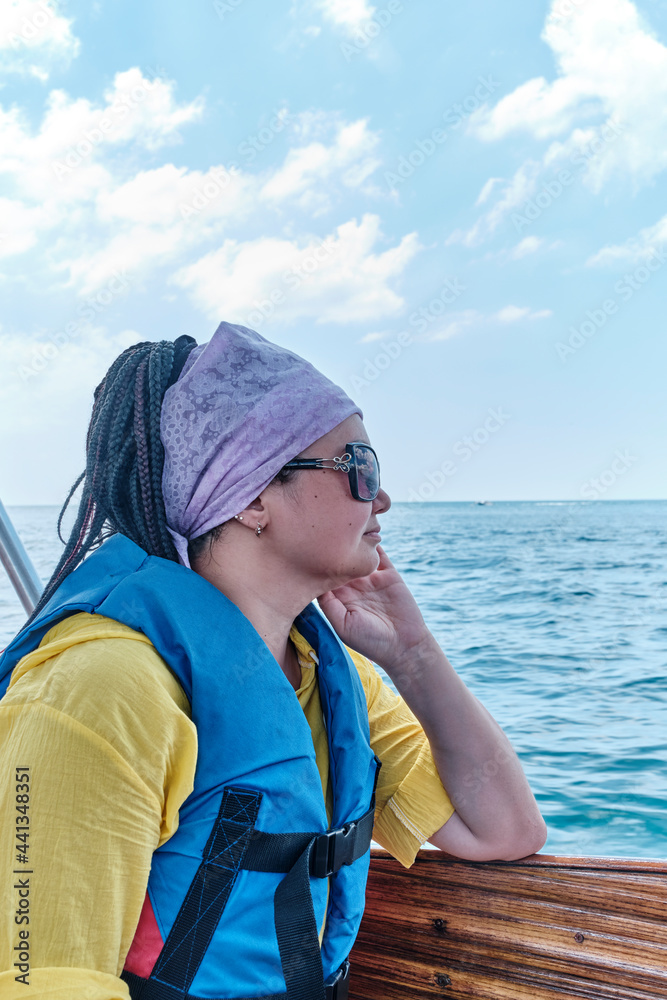 Young nice asian woman in life jacket and sunglasses on pleasure boat on sea.