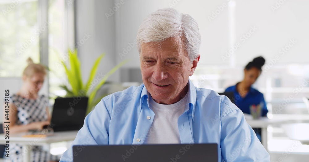 Aged caucasian businessman sitting at desk in office using laptop and drinking coffee Aged caucasian businessman sitting at desk in office using laptop and drinking coffee