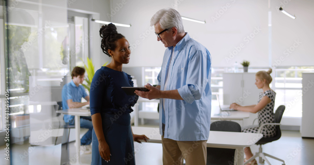 Obraz premium Diverse happy colleagues talk and use digital tablet in office.