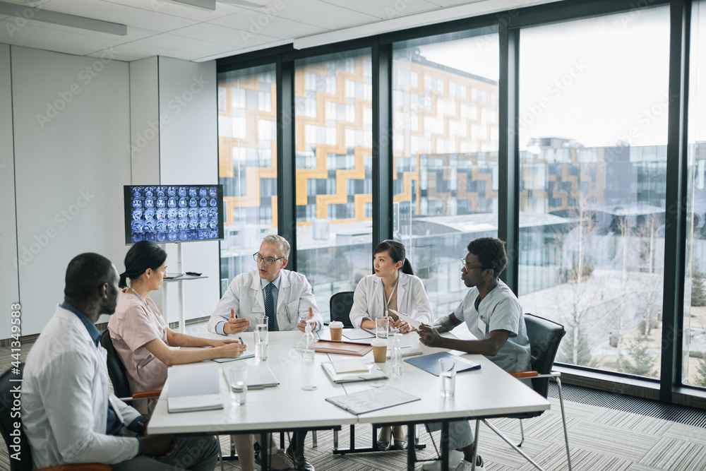 Wide angle view at doctors sitting at meeting table in conference room during medical council, copy space