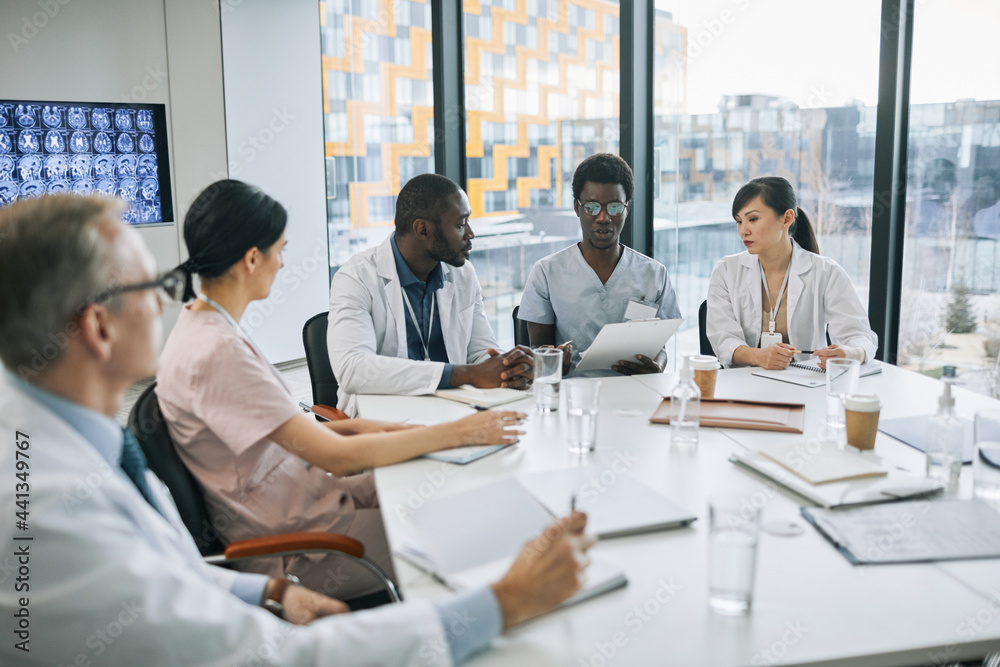Large group of doctors discussing case while sitting at meeting table during medical conference, copy space Large group of doctors discussing case while sitting at meeting table during medical conference, copy space