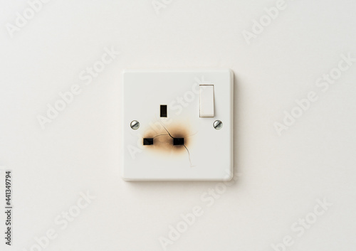 Broken electrical domestic power socket with cracks and burn marks on a white wall