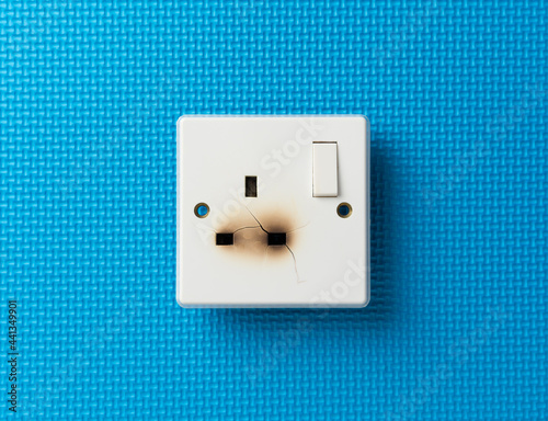 Damaged electrical wall power socket with burn marks and cracks on a blue background