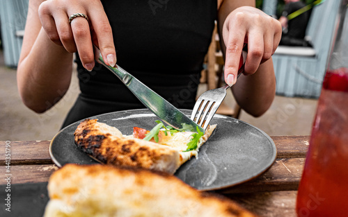 woman hands with knife and fork cutting pizza on table in cafe outdoor