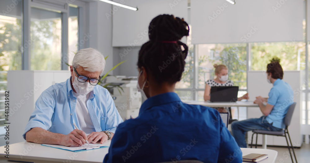 Obraz premium Mature male client in medical mask sign loan agreement in bank