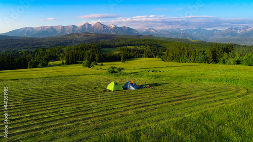 Camp in the mountains during sunrise, aerial view. Two tents in the middle of meadow with high mountains view. Tatra mountains in background. Concept: nomads, outdoor travelling, into the wild