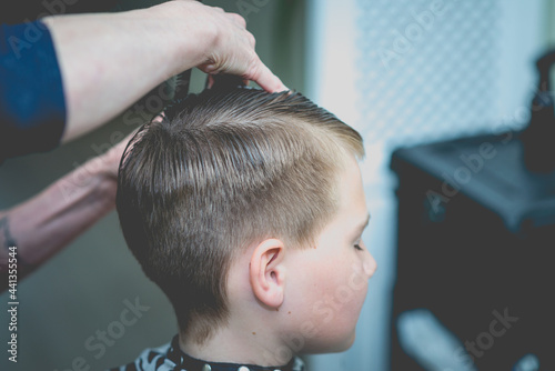 Cute little boy getting haircut by hairdresser at the barbershop.Side view.Closeup.Toned.