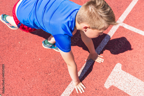 Caucasian boy,kid prepare to start running on a red track.young boy in starting position ready for running.Summer day.