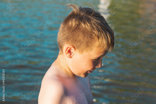 Cute young boy enjoy having fun at lake or river beach water on warm sunset evening time outdoors.Closeup. © ARVD73