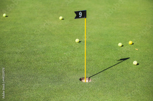 Flag in a golf hole on the background of green grass and golf balls. Golfing, golf club. 