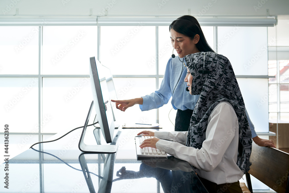 Two call center woman teamwork for help customer issue with headset and computer in office Two call center woman teamwork for help customer issue with headset and computer in office