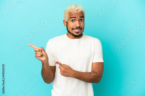 Young Colombian handsome man isolated on blue background frightened and pointing to the side