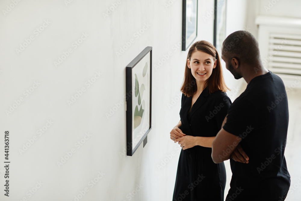 Fototapeta premium Side view portrait of elegant couple looking at abstract paintings in modern art gallery, copy space