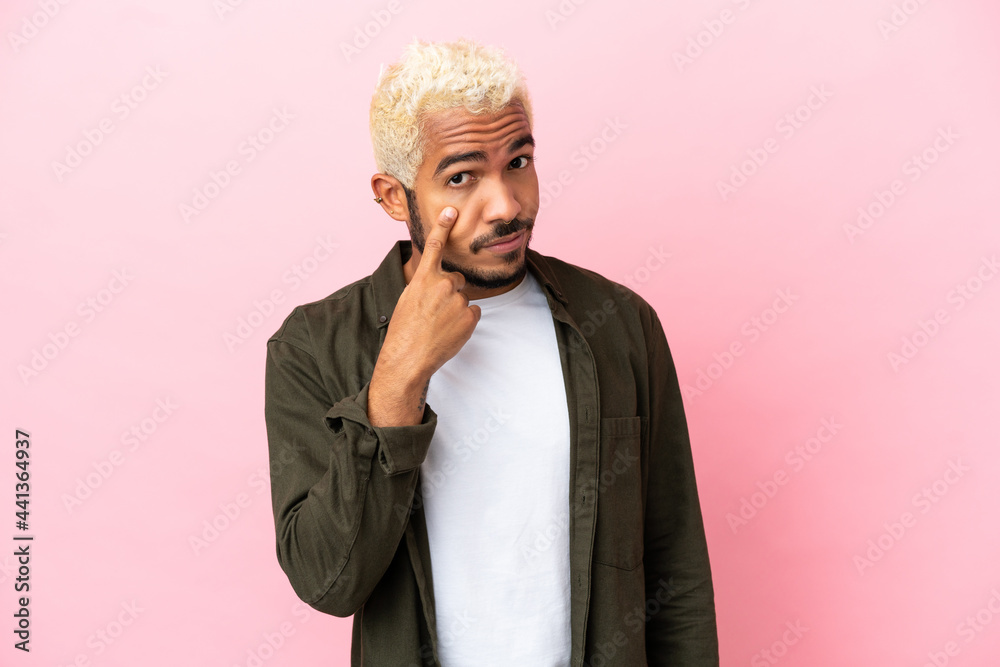 Young Colombian handsome man isolated on pink background showing something