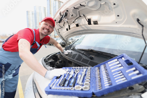 Smiling repairman in uniform fixing car with tools