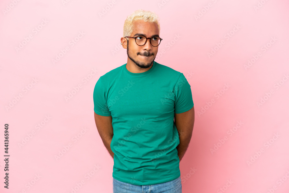 Young Colombian handsome man isolated on pink background having doubts while looking up Young Colombian handsome man isolated on pink background having doubts while looking up
